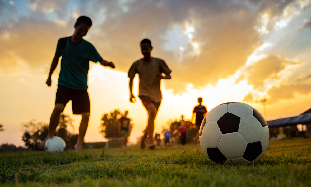 Two male adults playing football during sunset