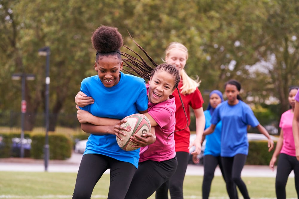 A photo of six females smiling and playing rugby outside
