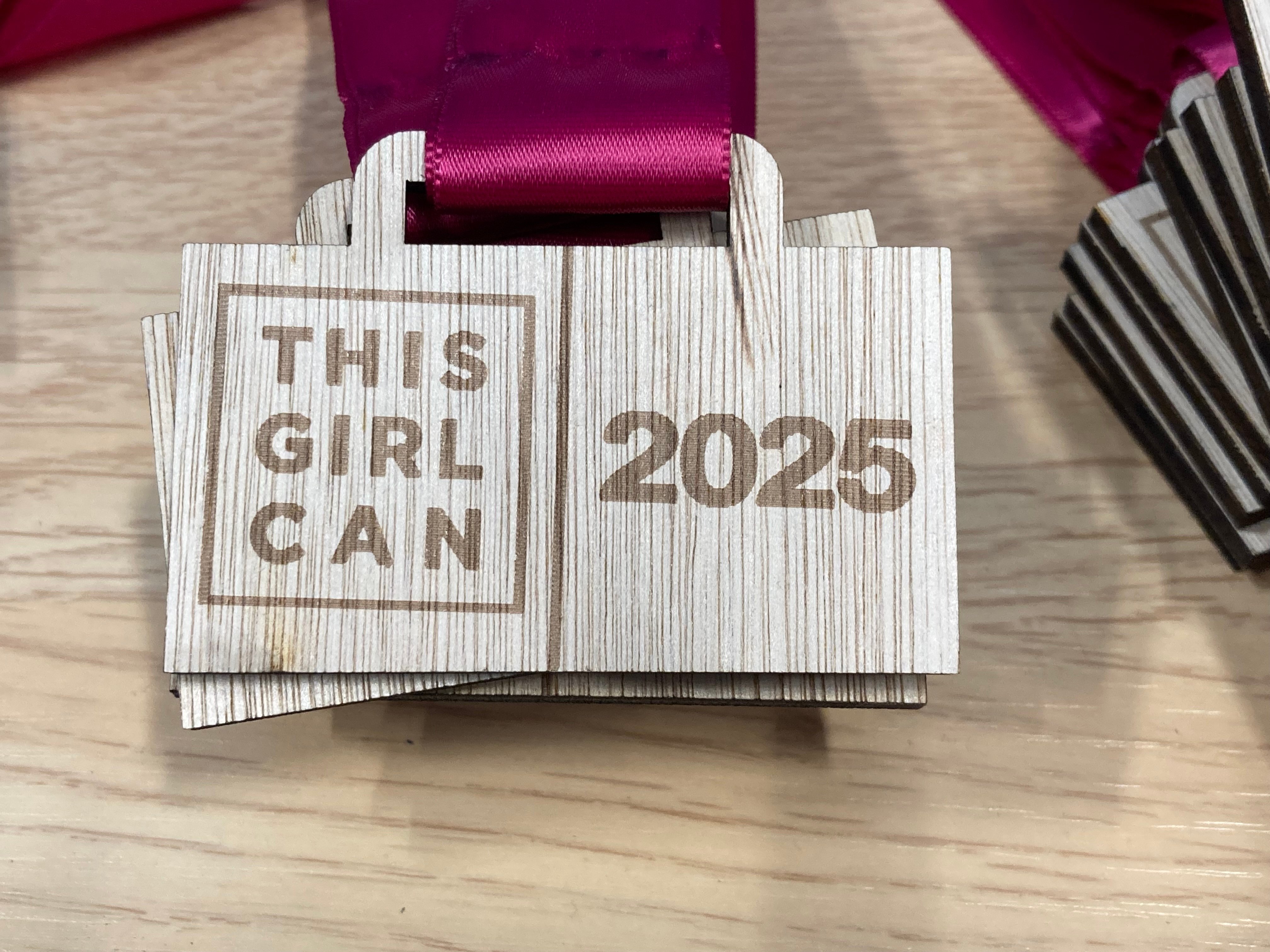 A photo of This Girl Can School Games wooden medals with a burgundy coloured ribbon